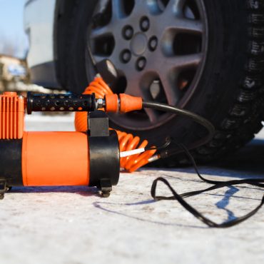 Car air compressor in working position at snow. Winter self-inflating wheels at the car in the field. The orange color, sunny winter day. Automobile tire pressure control.